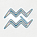 A die-cut sticker featuring the Aquarius zodiac symbol with a colorful patterned interior and the word 'AQUARIUS' printed diagonally, shown on a light textured background.
