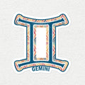 A die-cut vinyl sticker of the Gemini zodiac symbol, featuring a colorful geometric pattern in orange, pink, and blue on a white background with the word 'GEMINI' printed below, shown on a light textured wall.