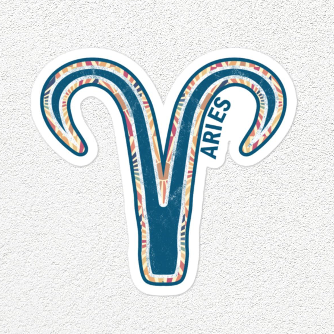 A die-cut vinyl sticker of the Aries zodiac symbol, featuring a teal blue and white patterned ram's head with the word 'ARIES' printed vertically, shown on a textured off-white background.