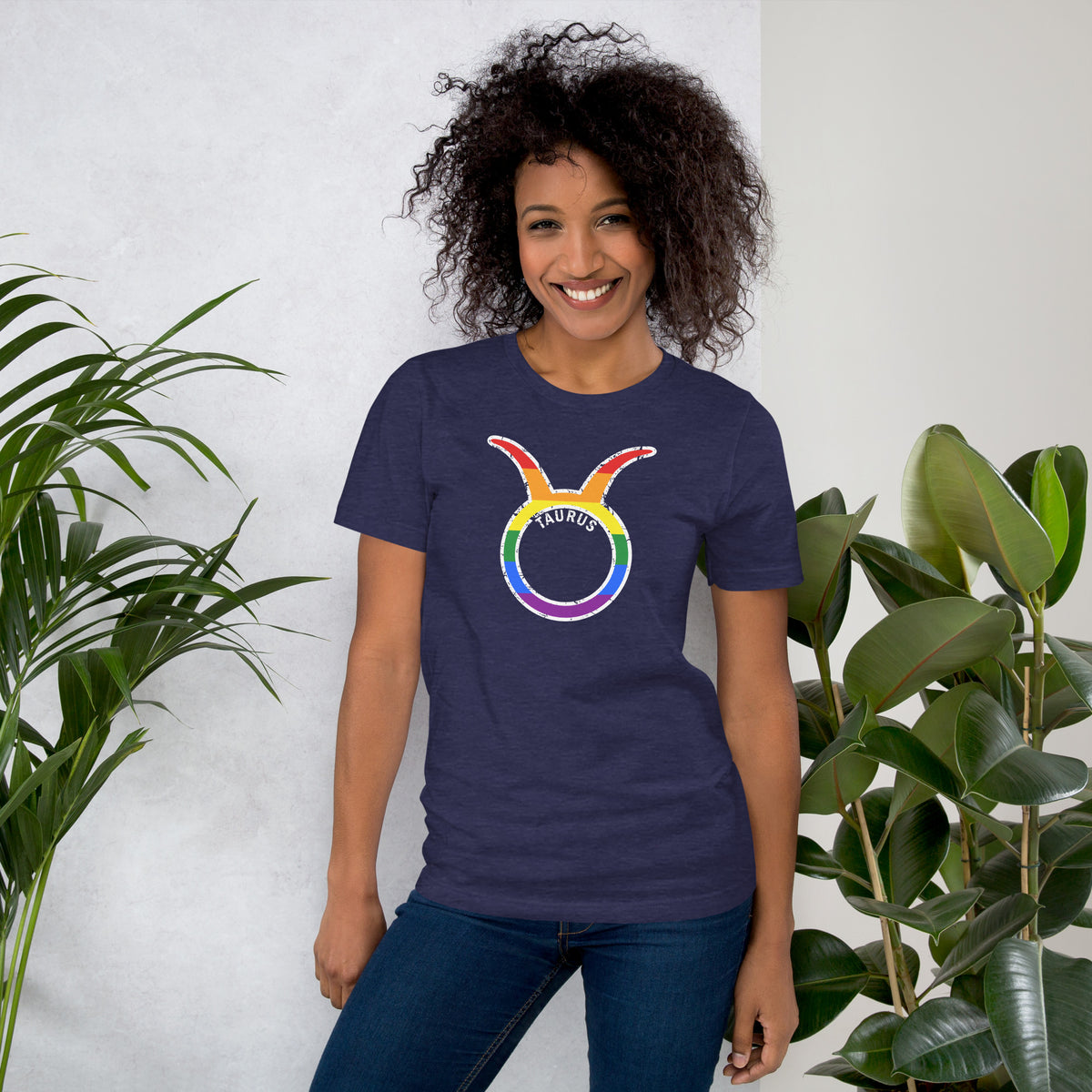 Person wearing a dark gray t-shirt with a rainbow Taurus astrology symbol with distressed graphics, against a white wall.